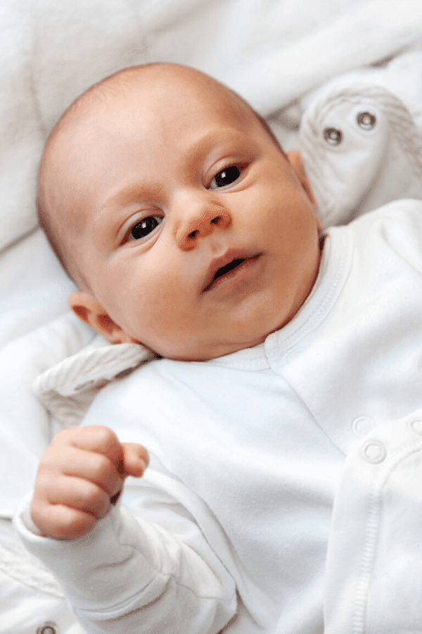 baby laying in cot, wearing a white babysuit.
