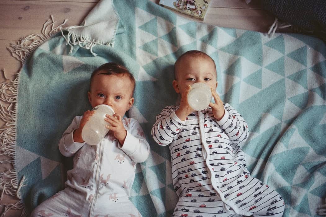 Two toddlers feeding from milk bottles