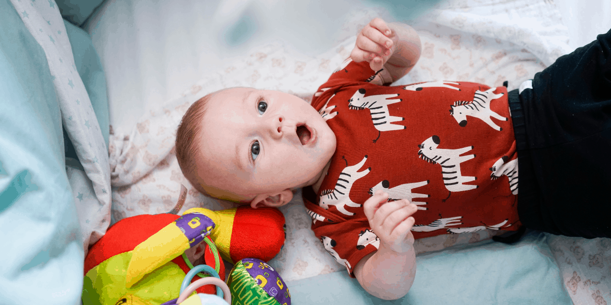 Baby is laying in his cot. He is wearing a red vest with Zebras.