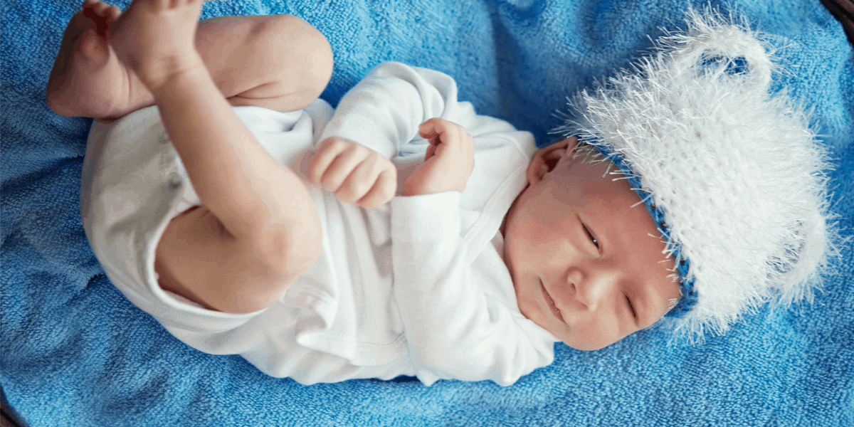 Baby laying on a blue towel. The baby is wearing a white fluffy hat