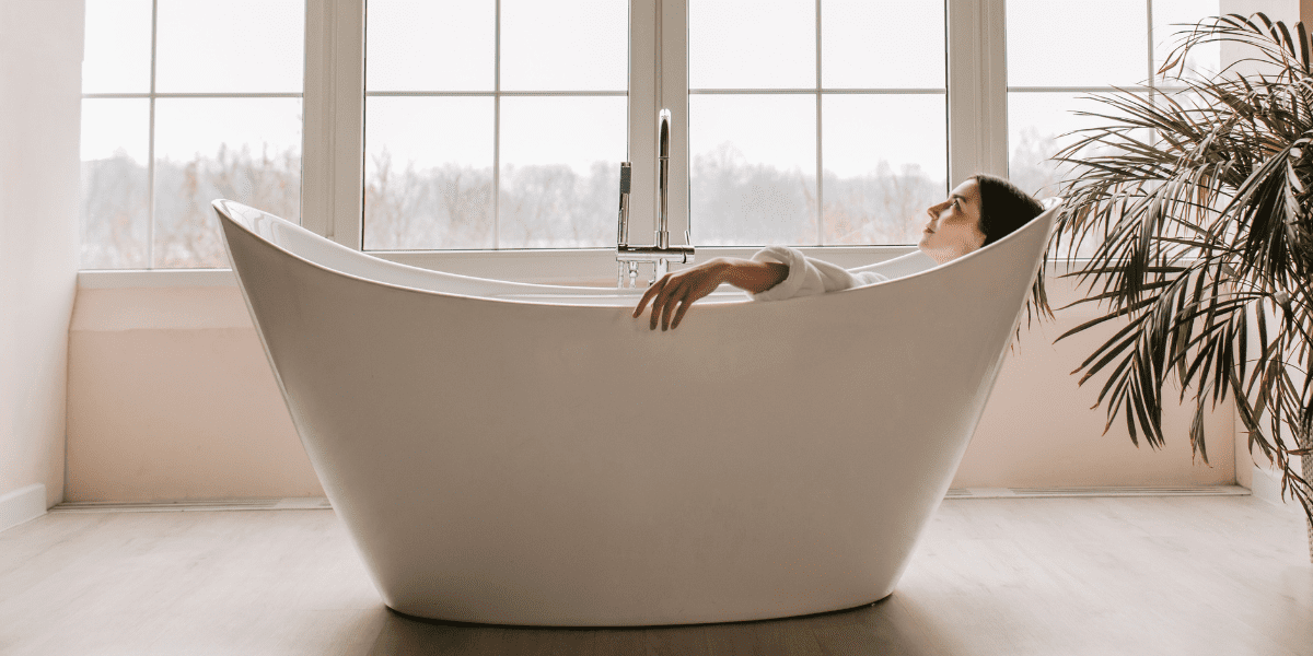 lady laying in free standing bath wearing a white robe