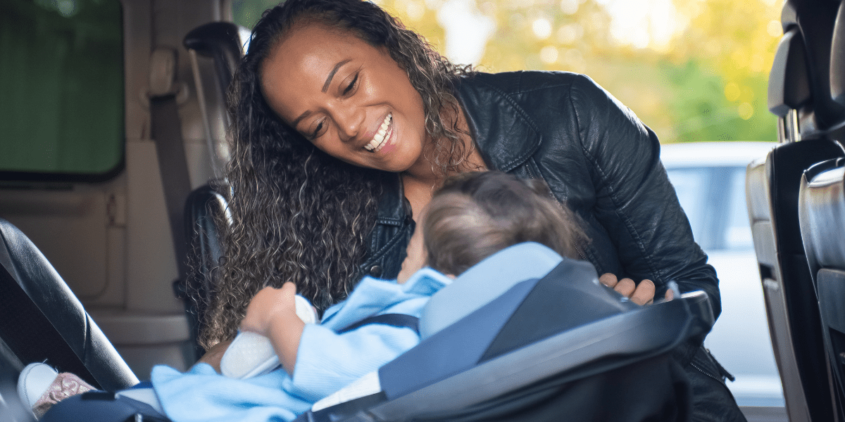 mother smiling at baby sitting in a rear facing car seat