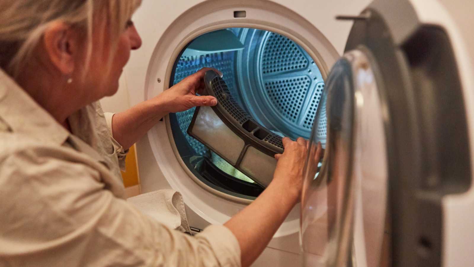 A housewife woman cleans the lint filter of the washing machine or tumble dryer